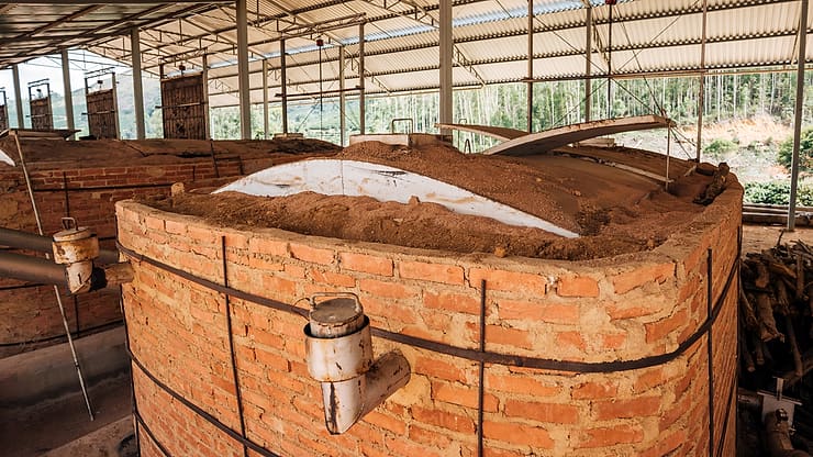 Top of a brick carbonisation kiln with its condenser outlet, under a steel roof